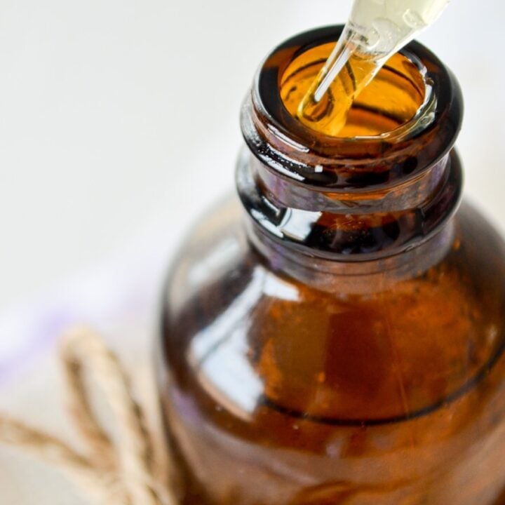 A close up of a amber jar with the dropper being removed; drops of facial serum dripping out.