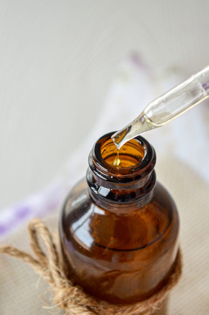 A close up of a amber jar with the dropper being removed; drops of facial serum dripping out.