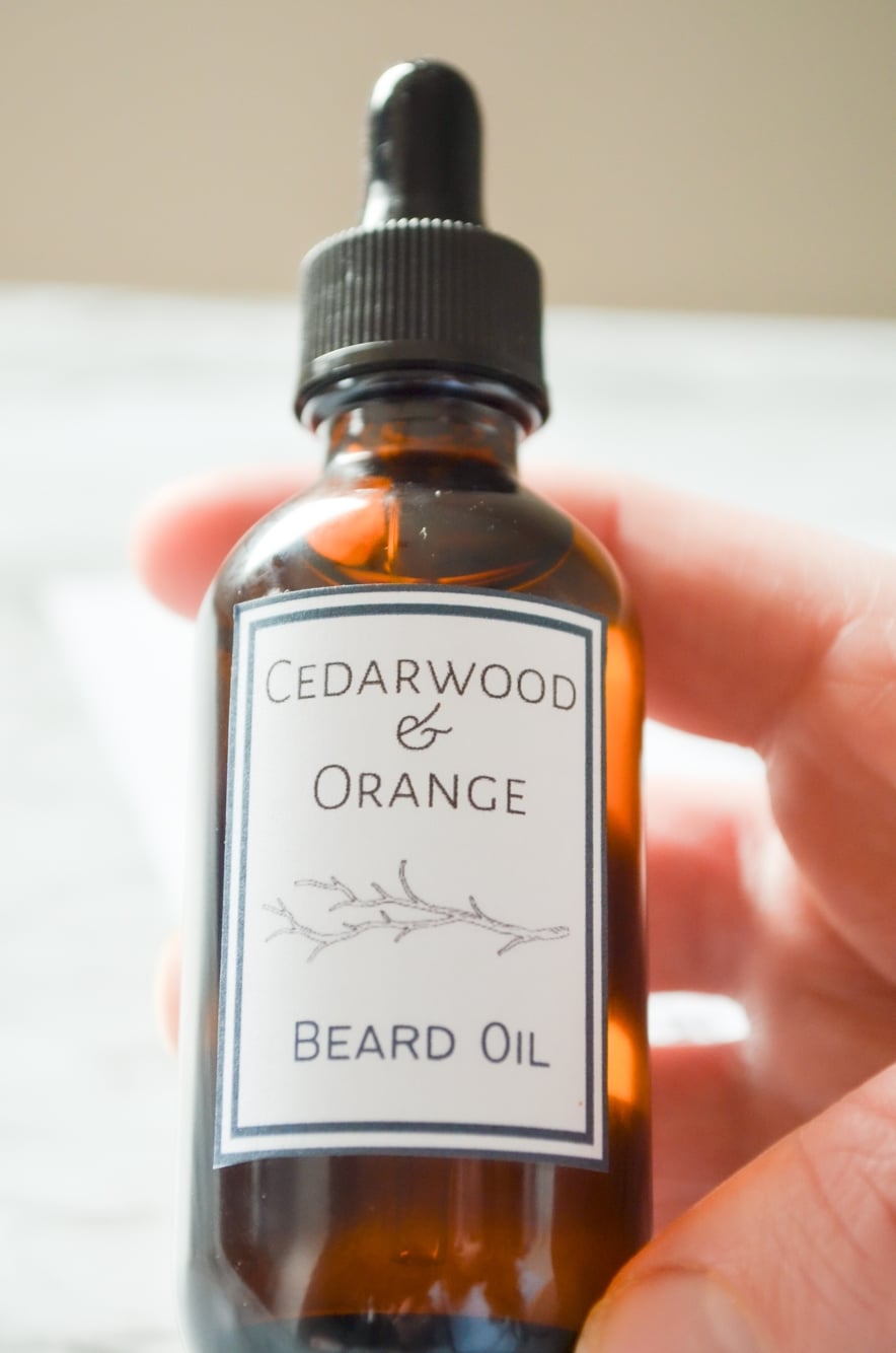 A bottle of Cedarwood and Orange Beard Oil being held by a close up hand.