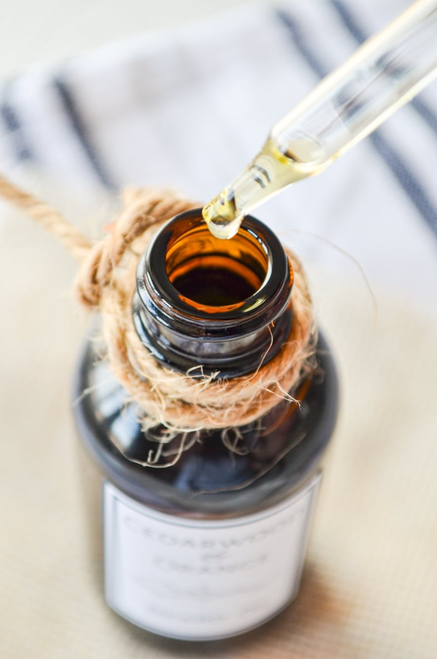 A close up of an amber bottle with a bit of twine tied around the top. A dropper with some oil coming out of the bottle.