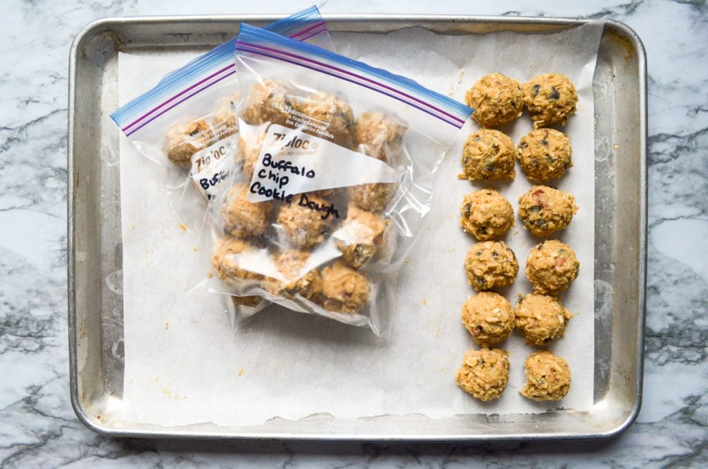 A baking sheet with cooking dough portioned to the right, and freezer bags with frozen dough in the center of the sheet.