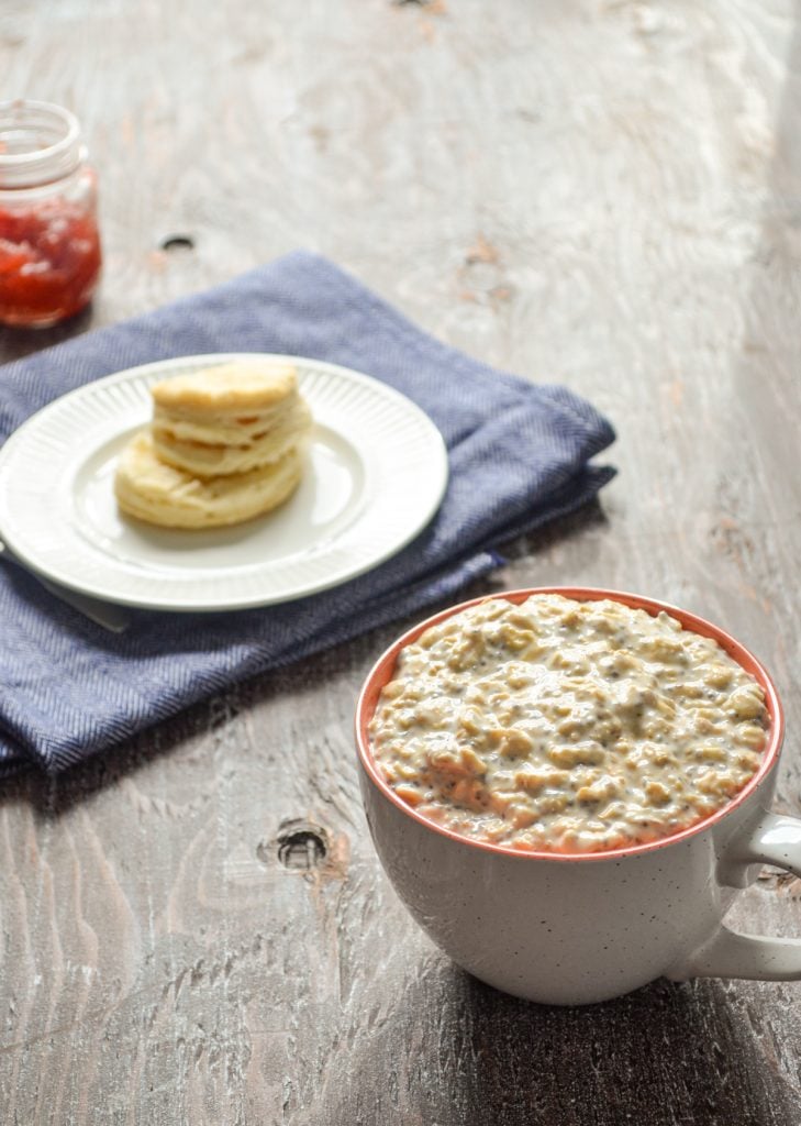 A mug of overnight oats, with a biscuit and some strawberry preserves in the background.