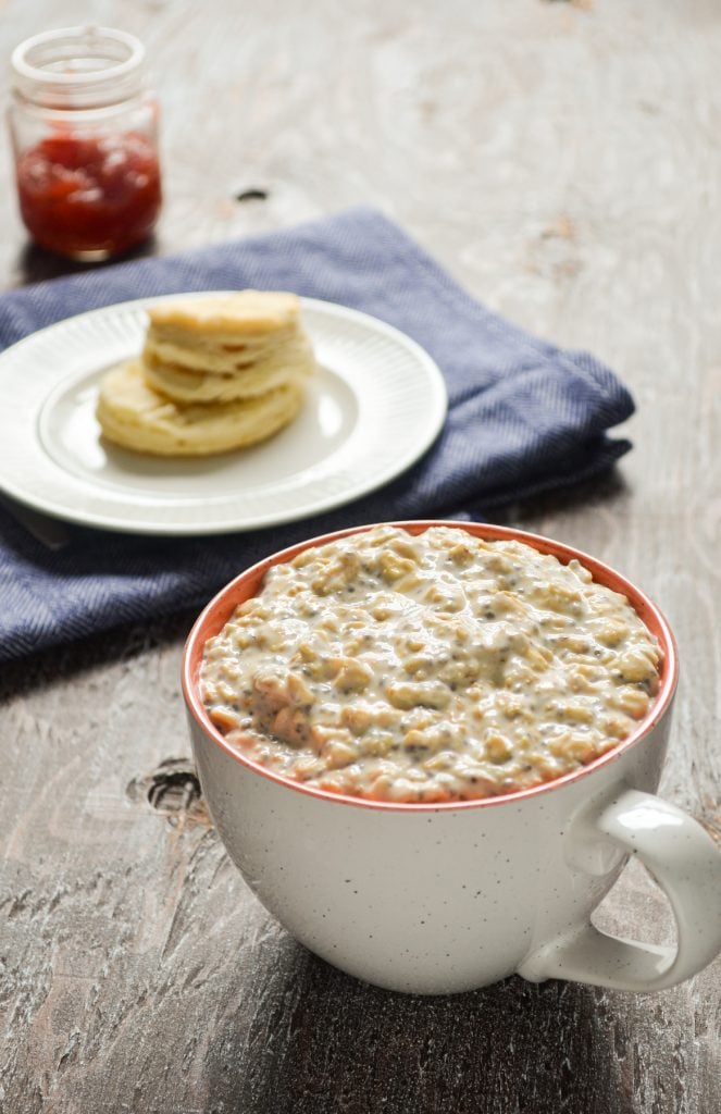 A mug of overnight oats, with a biscuit and some strawberry preserves in the background.