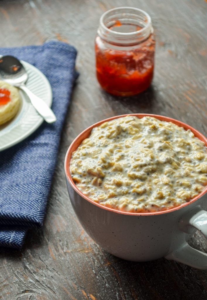 A mug of overnight oats, with a biscuit and some strawberry preserves in the background.