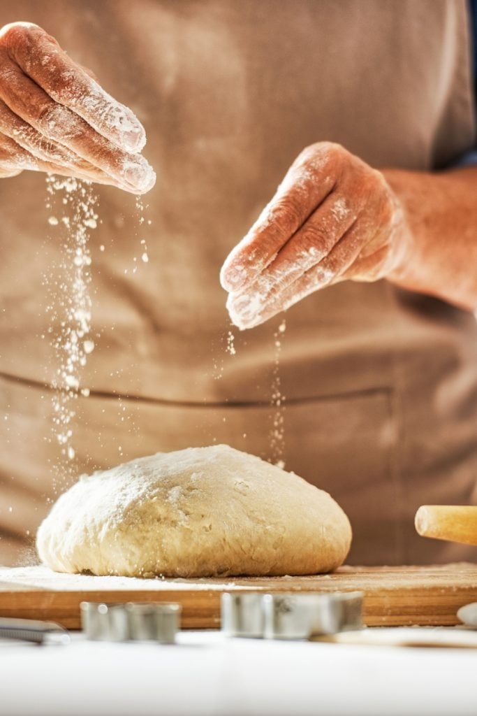 Hands sprinkling flour on bread dough.