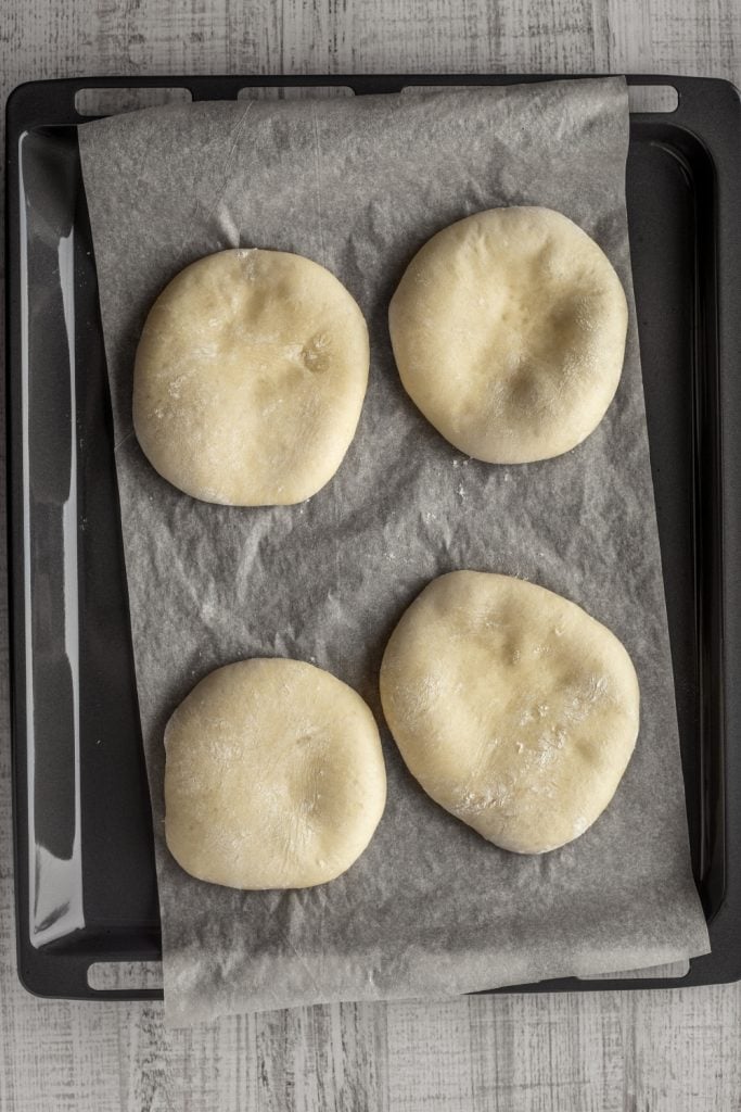 Four buns on a parchment lined baking sheet.