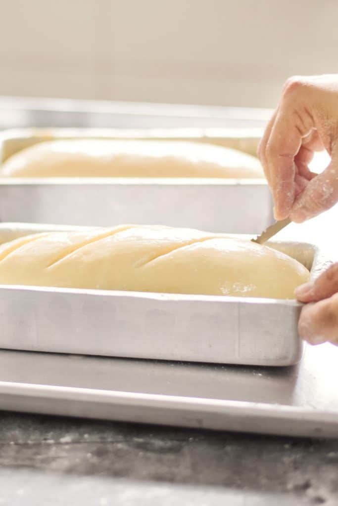 A baker cutting a loaf of bread with a sharp razor.