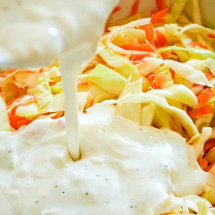 A close up of buttermilk coleslaw dressing being poured on top of shredded cabbage and carrots.
