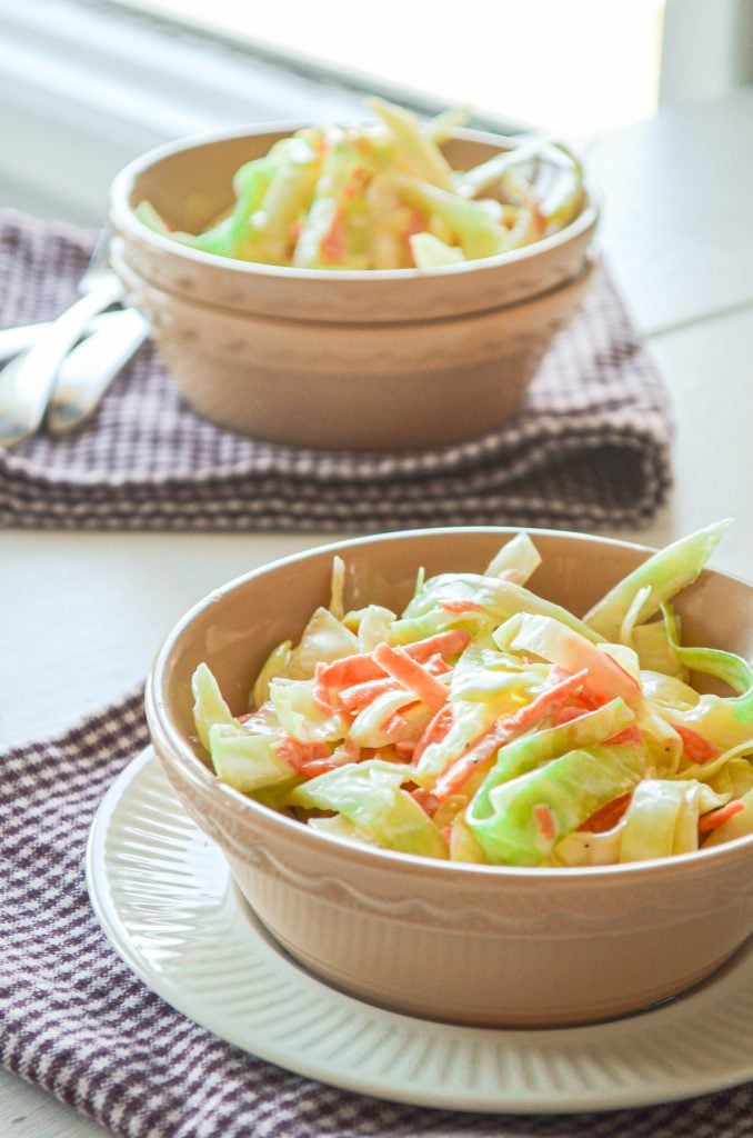 Two bowls of coleslaw are resting on purple check napkins.