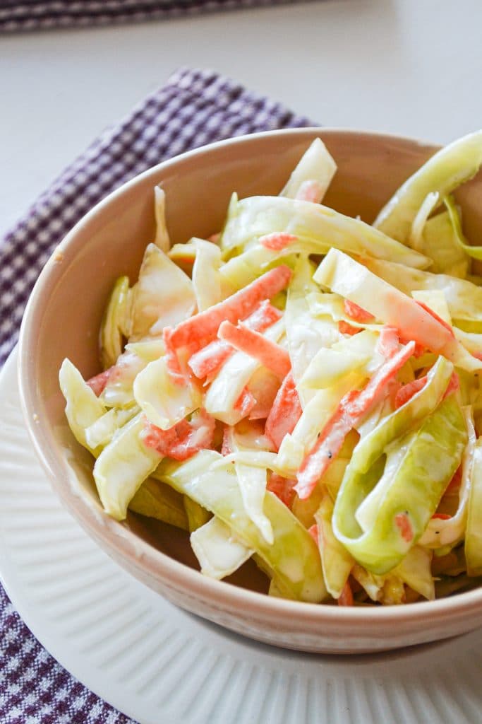 A close up of a bowl of buttermilk coleslaw, resting on a purple check napkin.