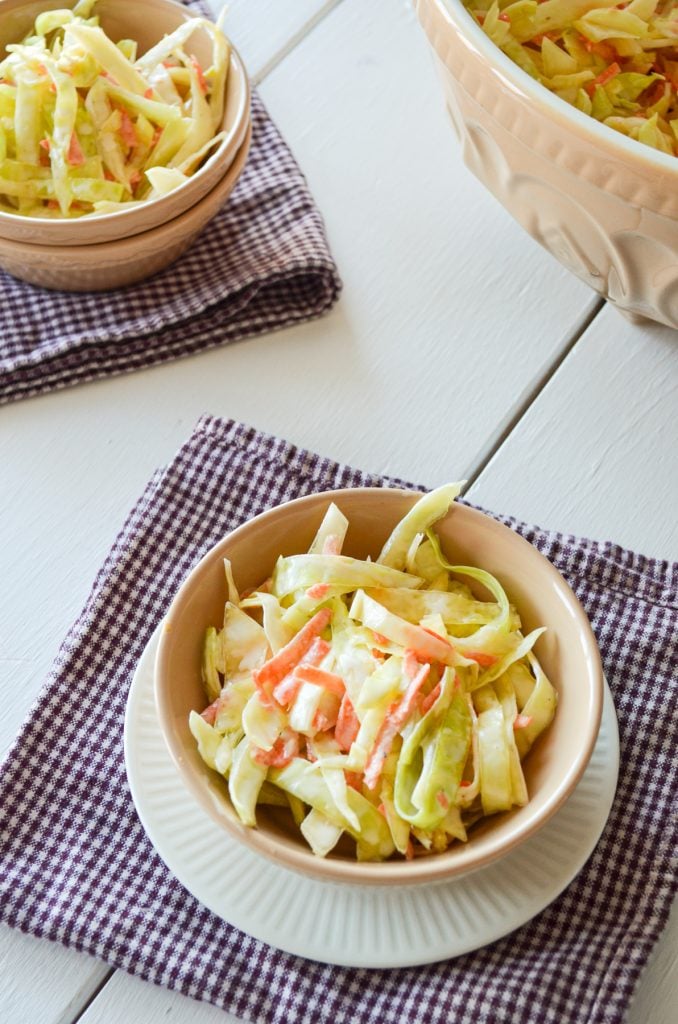 A bowl of coleslaw on a purple check napkin. A second owl in the top left corner. 