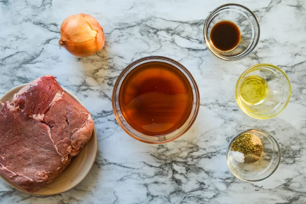 The ingredients needed to make Crockpot French Dip Sandwiches: beef, beef broth, seasonings, onion, worcestershire sauce, and oil. 