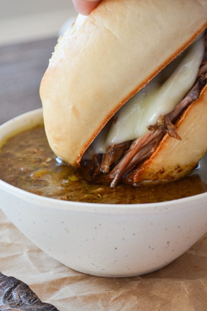 A french dip sandwich being dipped into au jus.