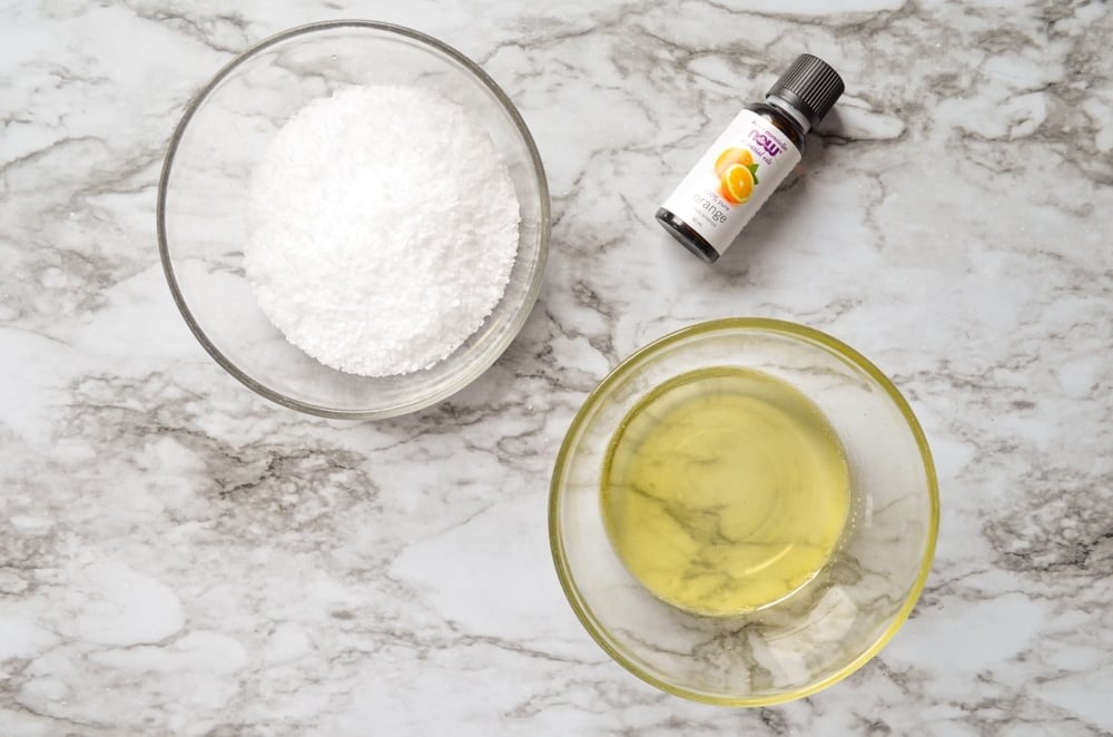 An overhead view of the ingredients needed for Facial salt scrub: Coconut oil, jojoba oil, orange essential oil, and coarse salt.