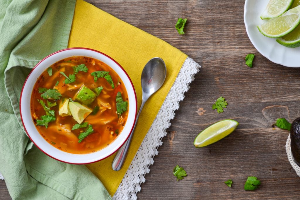 A bowl of soup on a yellow napkin, garnished with avocado and cilantro.