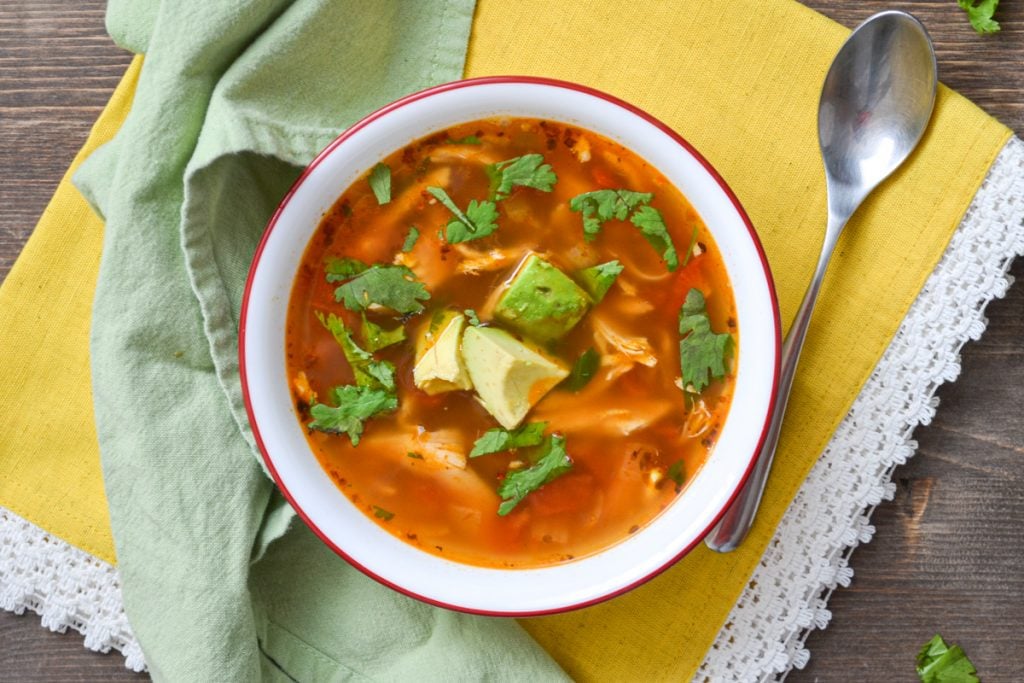 A bowl of healthy mexican chicken soup, resting on a yellow napkin.