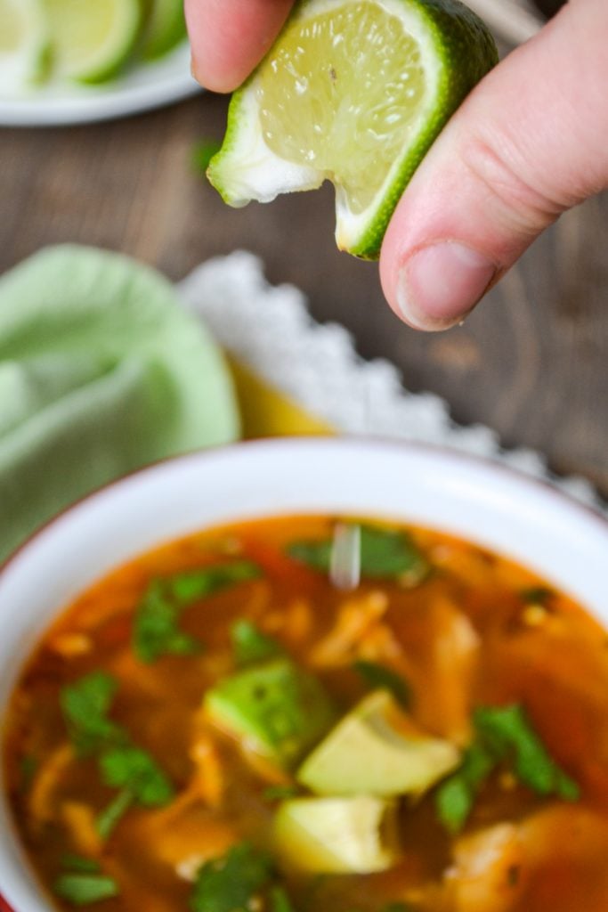 A fresh lime wedge being squeezed into a bowl of Mexican Chicken Soup.