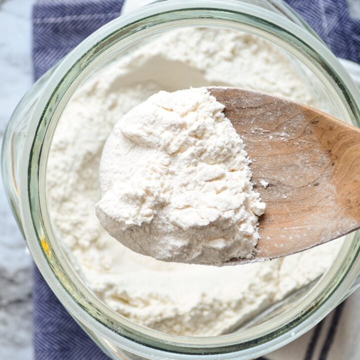 Bread flour being scooped from a glass canister.