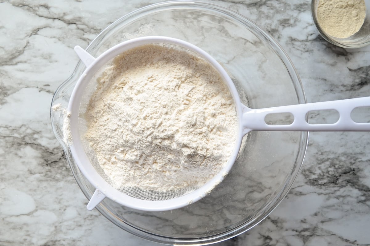 Flour in a fine mesh sieve set over a glass bowl.