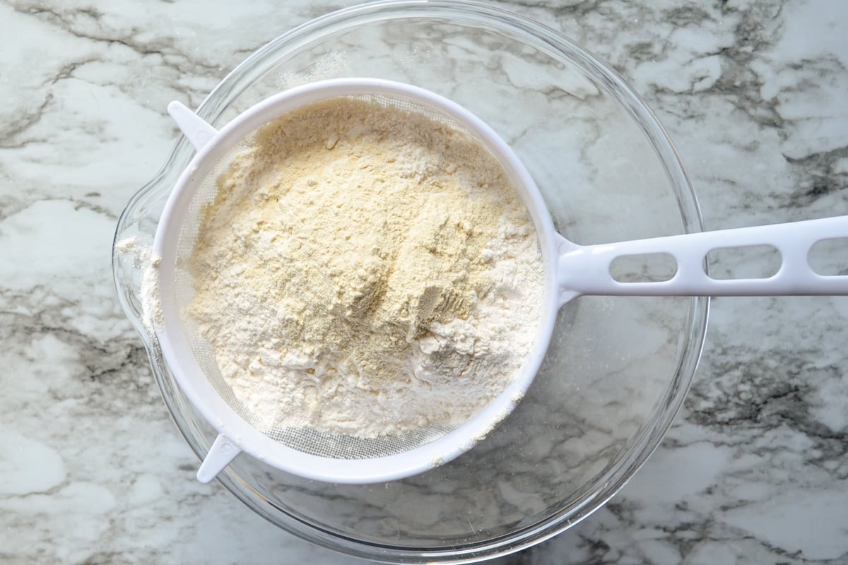 Flour and wheat gluten in a fine mesh sieve set over a glass bowl.