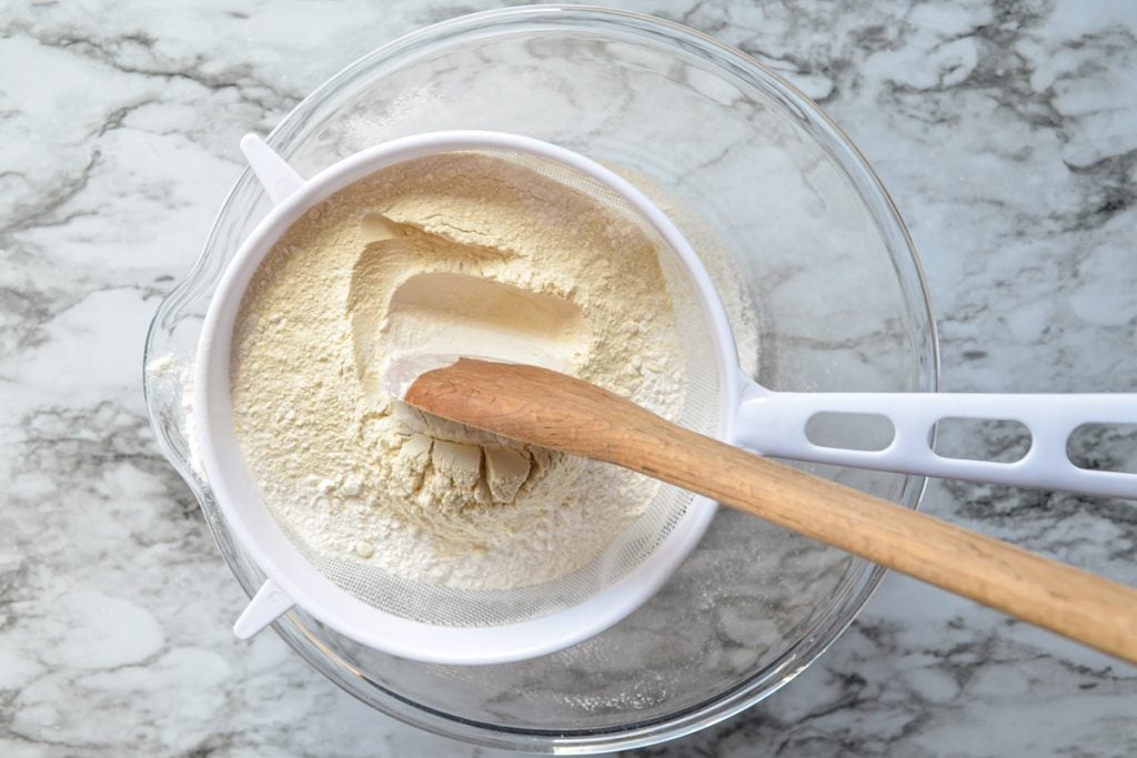 A fine mesh sieve with flour and wheat gluten, being worked by a wooden spoon.