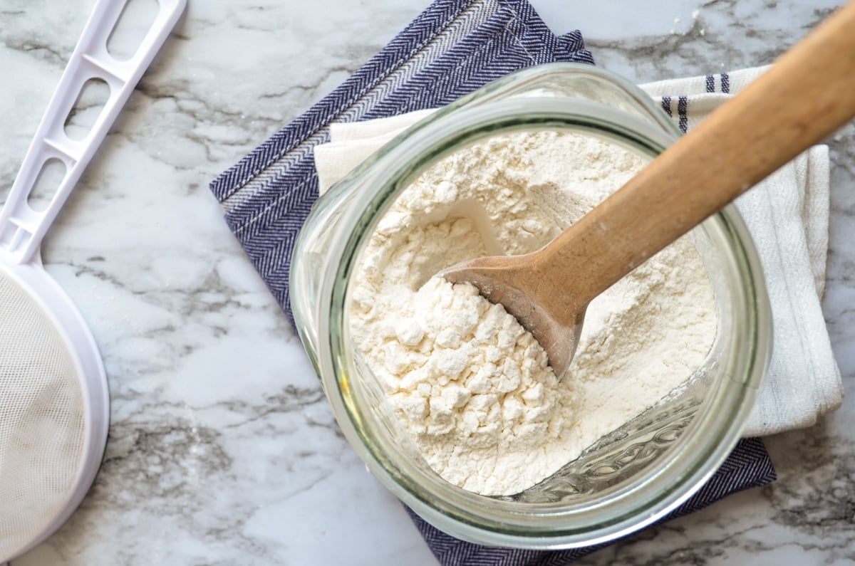 A glass canister of flour on a blue napkin and a marble counter.