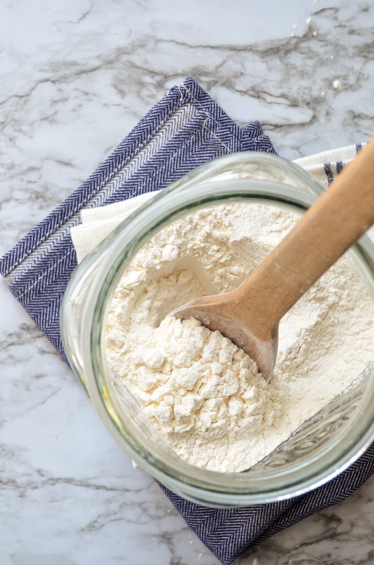 A glass canister of flour on a blue napkin and a marble counter.