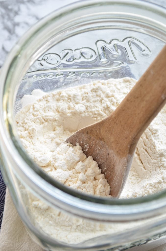 Flour in a large glass canister with a wooden spoon in it.