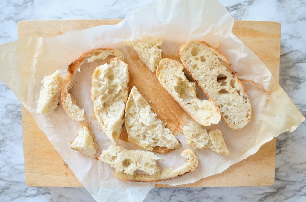 Random pieces of bread lay on top of a wooden cutting board.