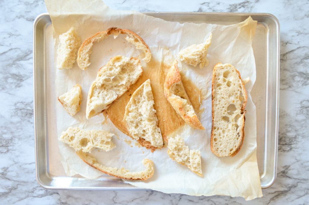 Random pieces of sourdough bread spread on a baking sheet, ready to become sourdough breadcrumbs.