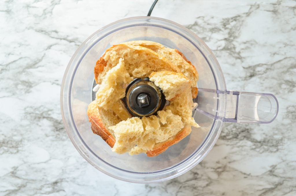 A food processor with leftover sourdough bread pieces in the bowl portion.