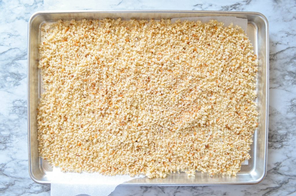 Breadcrumbs spread out on a sheet pan lined with parchment paper.