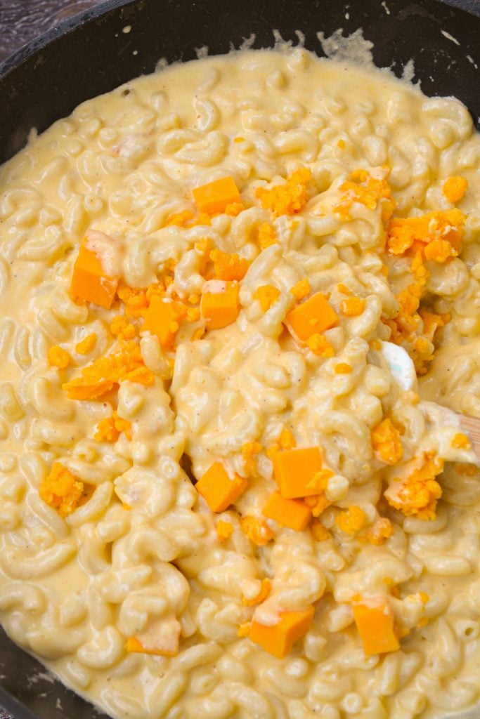 Macaroni being tossed with cheese cubes.