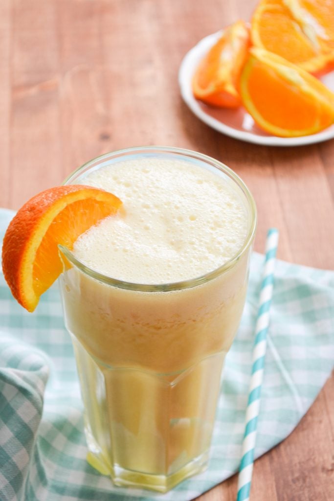 A large glass of an orange smoothie rests on a gingham napkin.