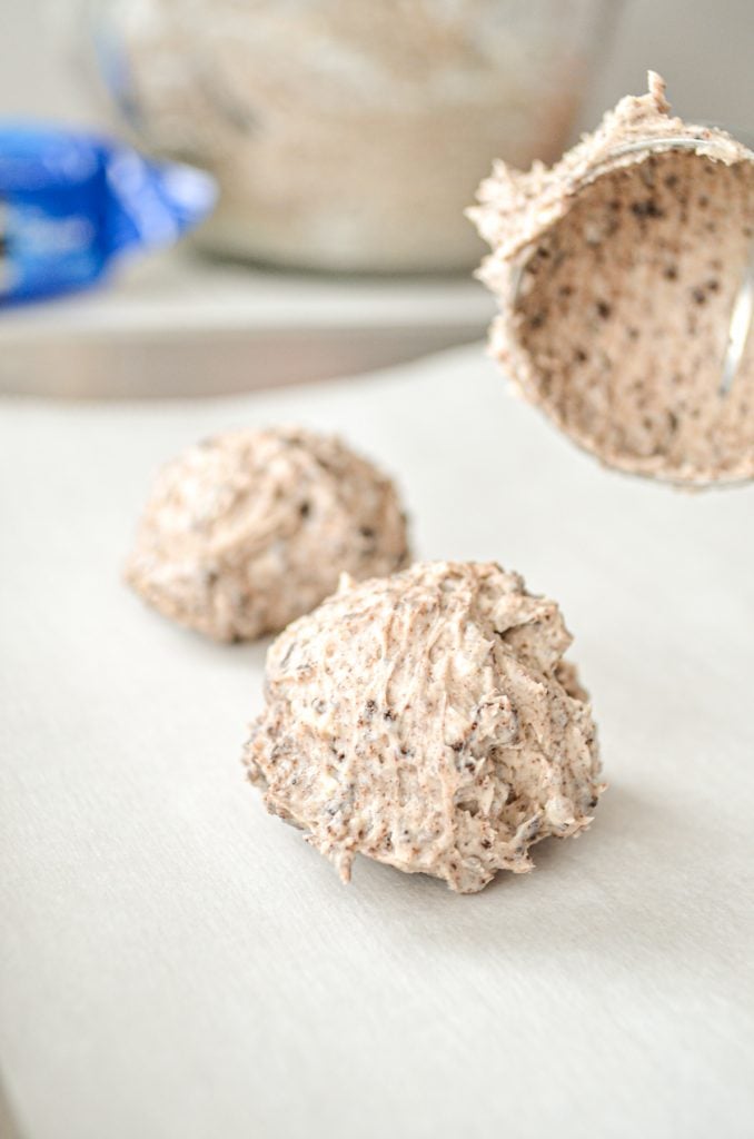 A cookie scoop, portioning out oreo cheesecake bites onto a lined baking sheet.