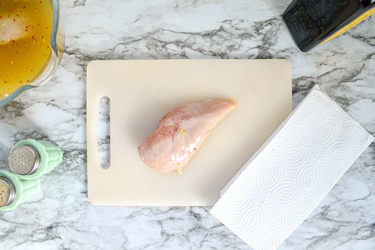 A chicken breast resting on a cutting board, with a paper towel to the side.