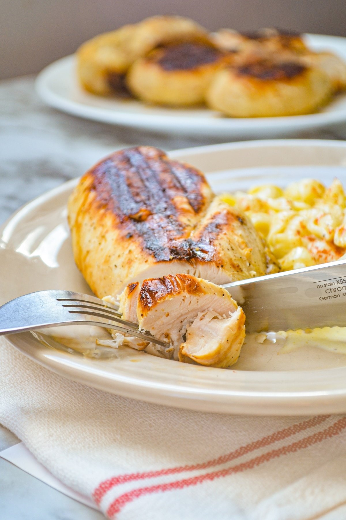 A grilled chicken breast being cut into with a knife.