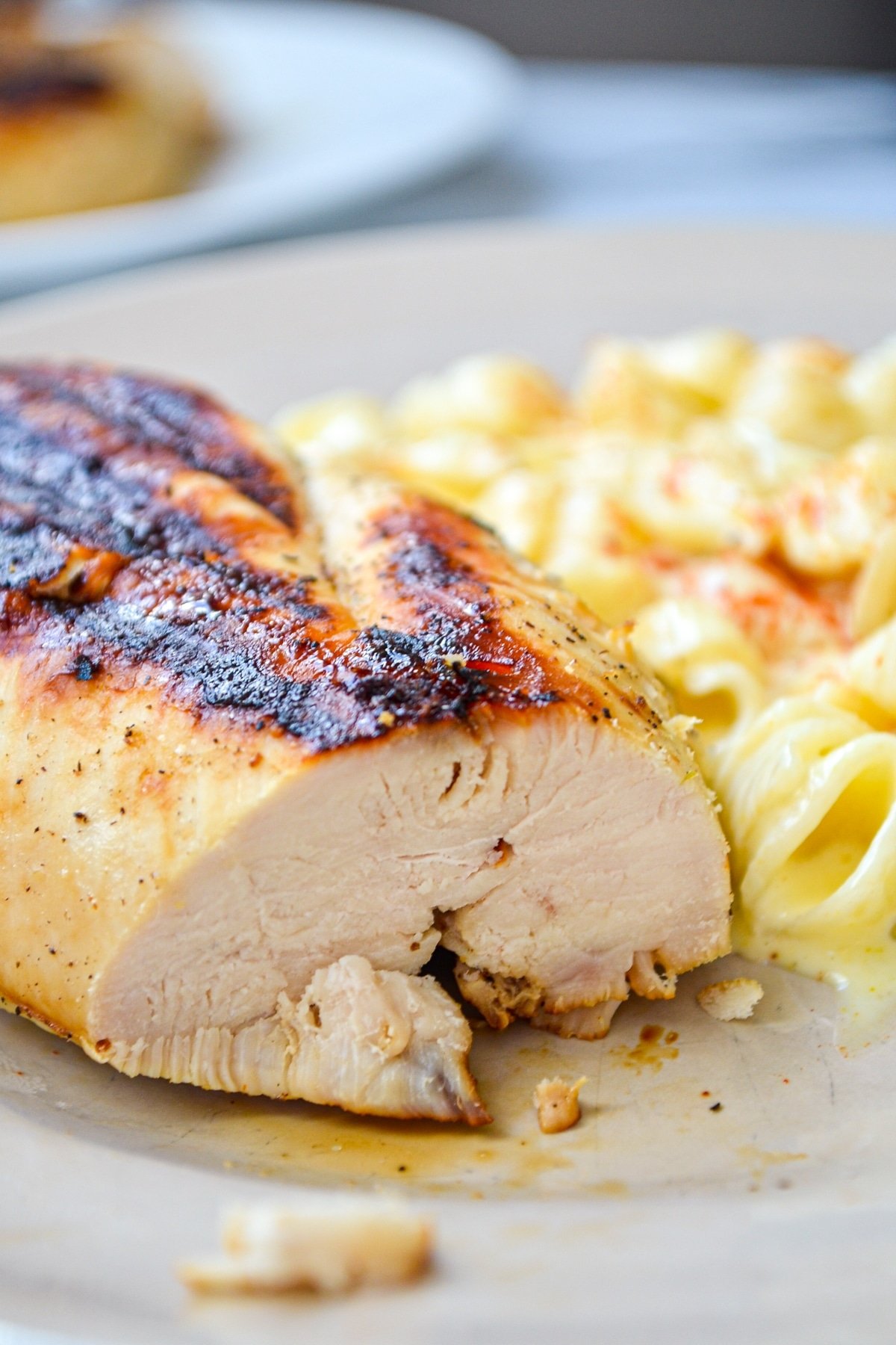 A close up of a piece of grilled chicken with macaroni salad on the side.