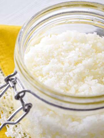 A close up of a jar of salt scrub, resting on a bright yellow cloth.