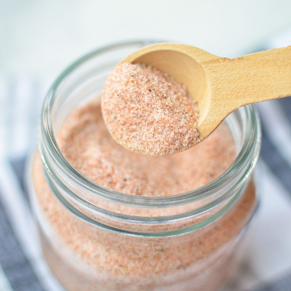 A jar of a homemade blend, of seasonings, with a wooden measuring spoon taking out a portion.