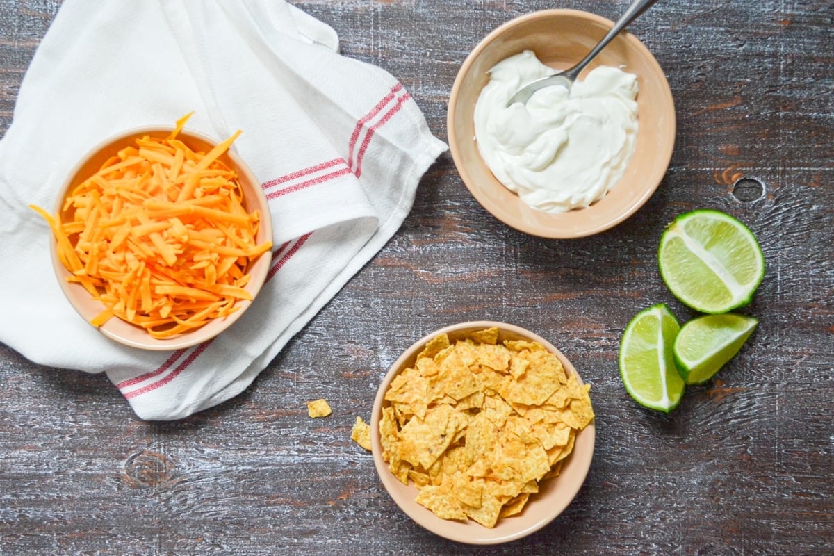 Topping suggestions for chicken taco soup include shredded cheese, crushed tortilla chips, sour cream, and lime wedges.