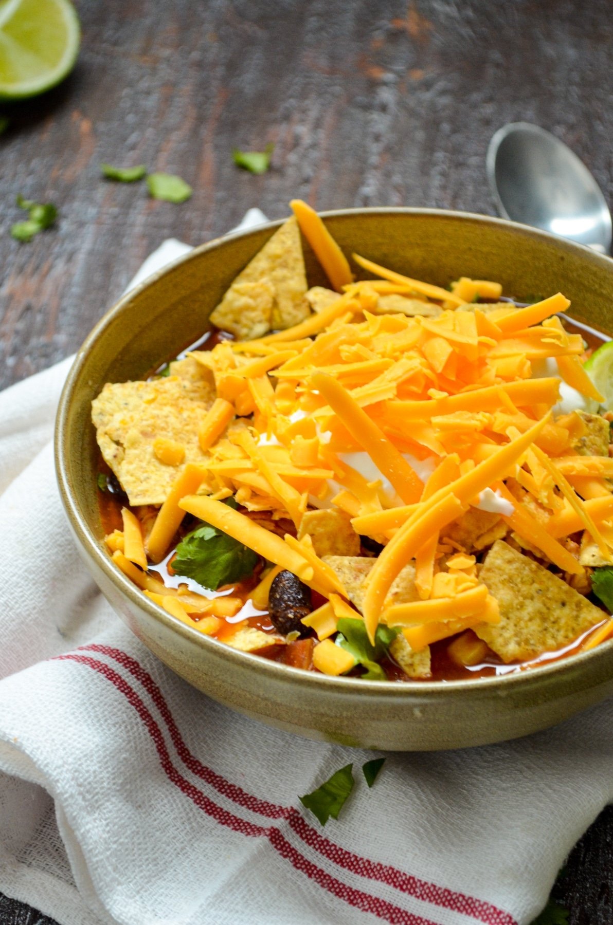 a bowl of chicken taco soup with shredded cheese and crushed tortilla chips on top.