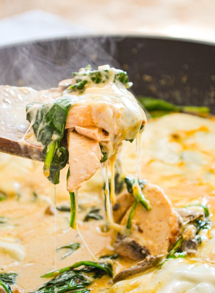 Spinach, mushroom and chicken skillet meal, with a wooden spoon pulling up a portion.