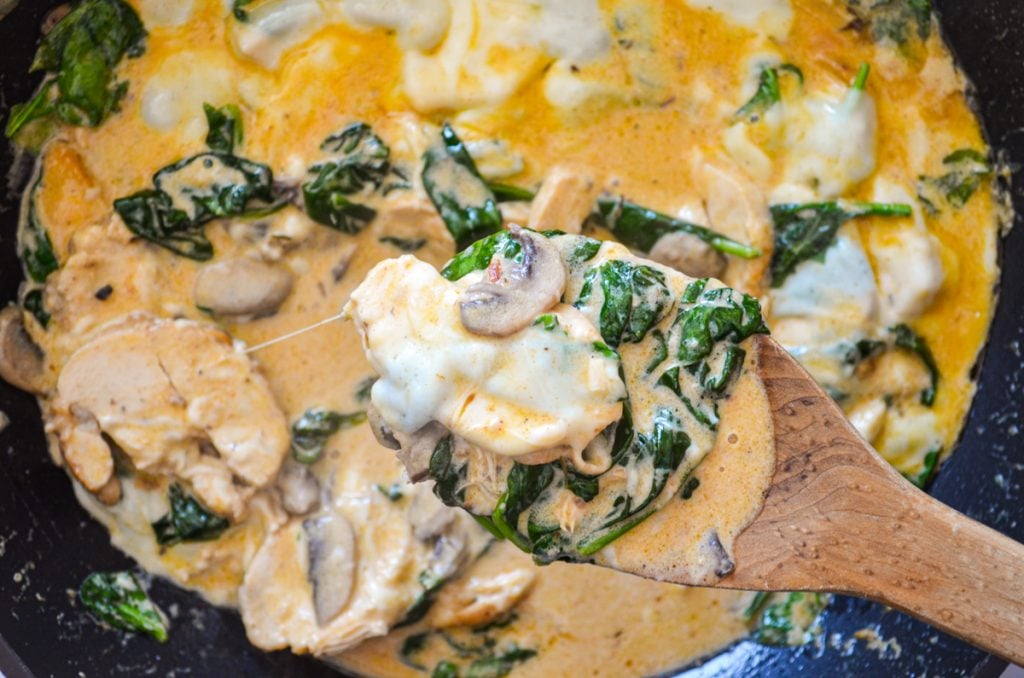 A low carb spinach, mushroom, and chicken skillet being pulled up with a wooden spoon.