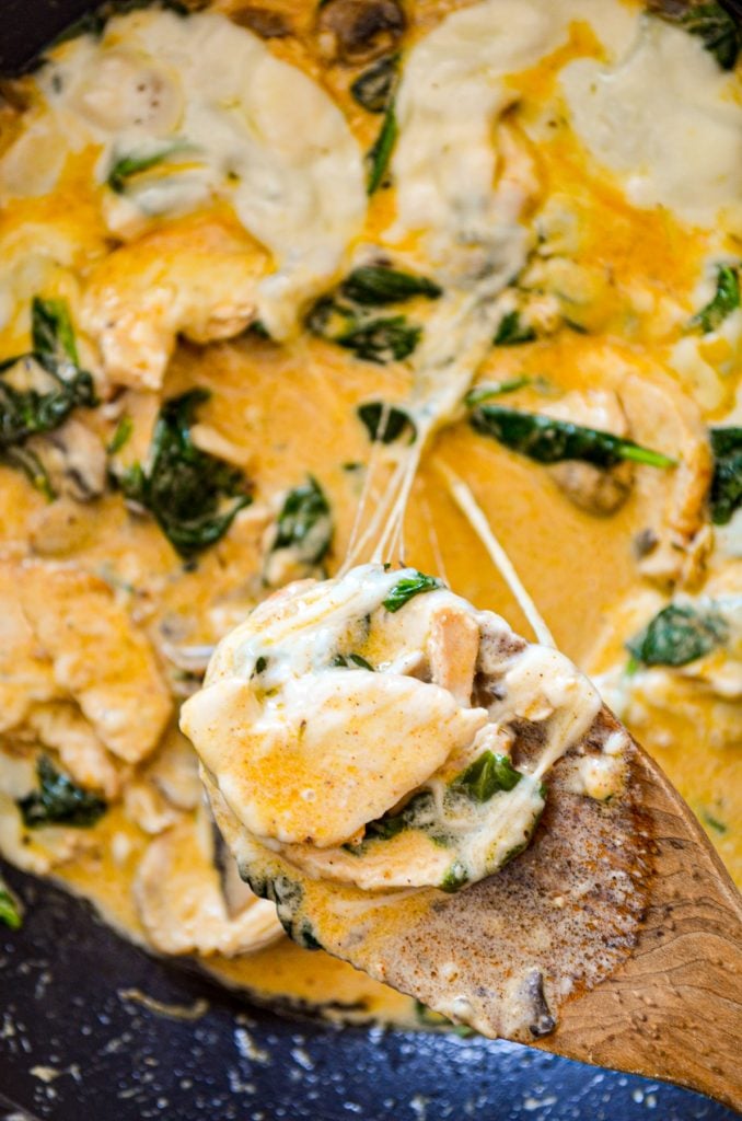 A wooden spoon pulling up a portion of a low carb skillet meal, the cheese stretching.