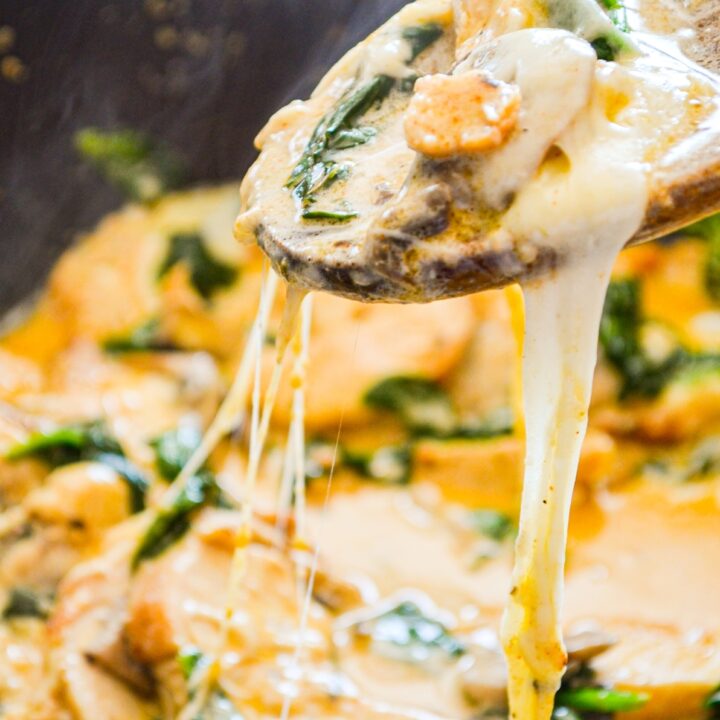 A wooden spoon pulls out a portion of Spinach, Mushroom, and Chicken skillet.