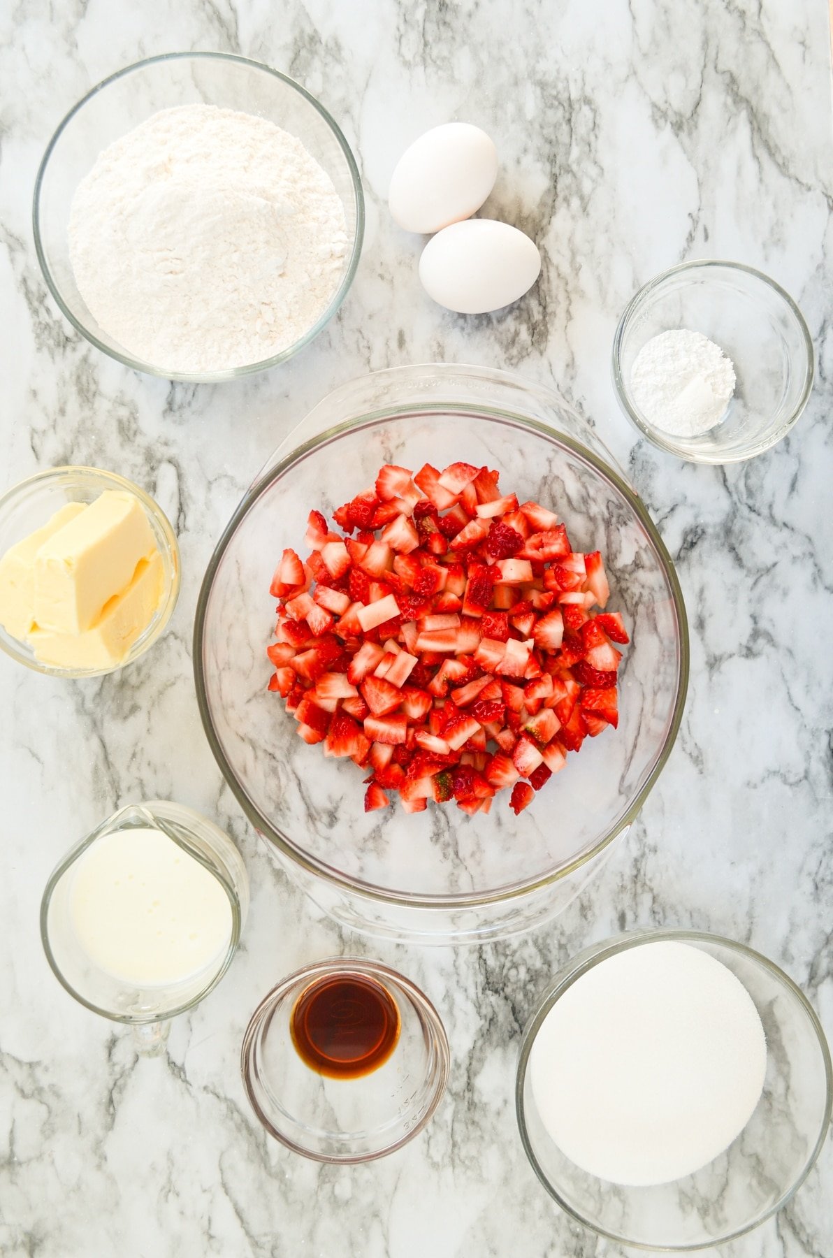 An overhead view of various ingredients including diced strawberries, butter, sugar, flour, vanilla, and salt. 