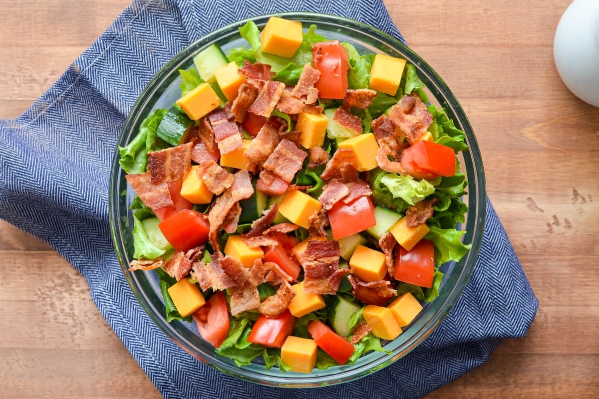 A salad topped with bacon, tomato, and cheese