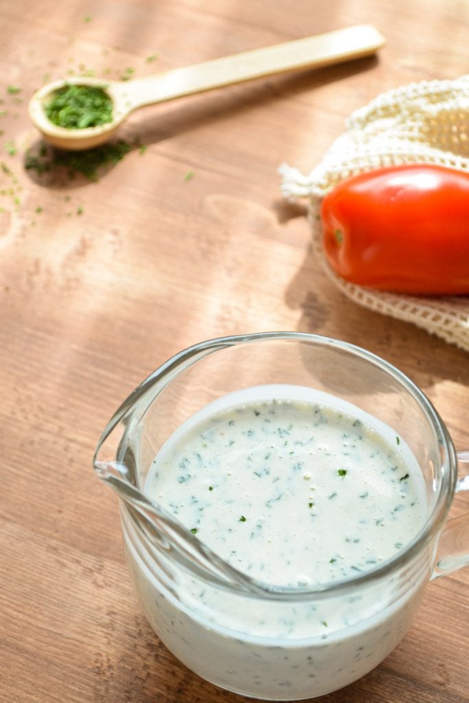 A small pouring glass of homemade dressing on a wood background.