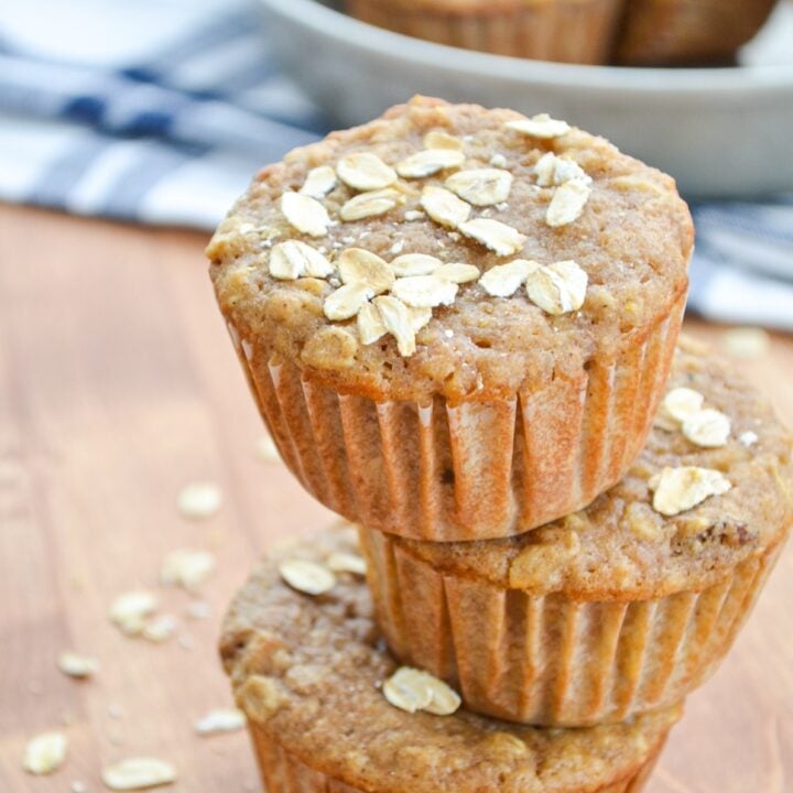 3 sourdough applesauce muffins stacked on top of each other with oatmeal sprinkled on top.